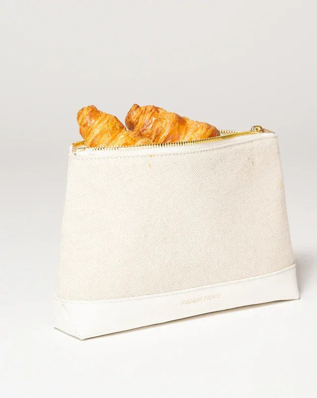 Cream canvas lunch bag with croissants, gold zipper, and vegan leather base for stylish picnics