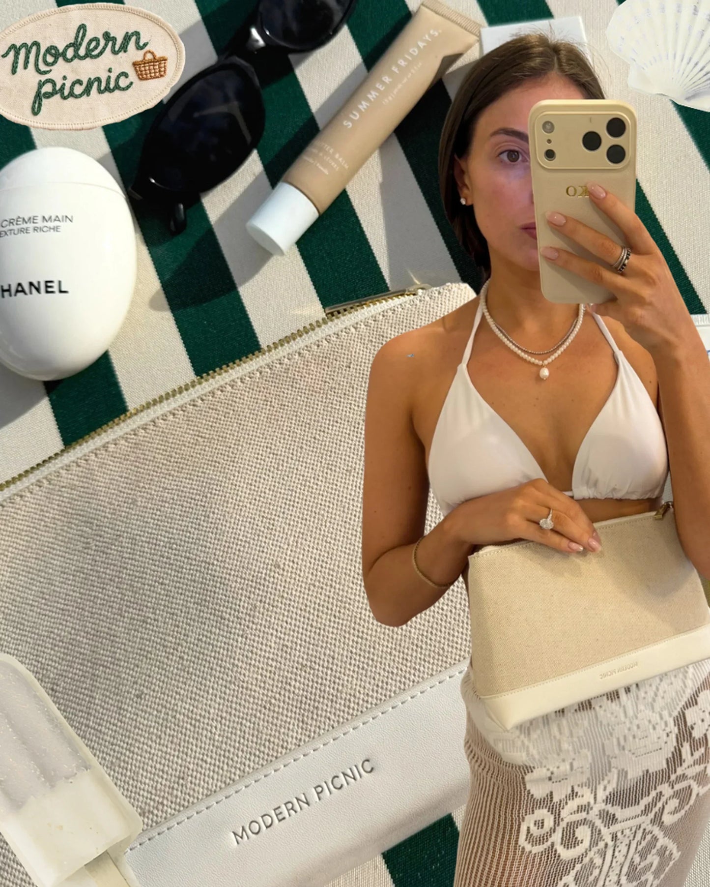 Stylish woman holding a chic beige clutch on a green-and-white striped picnic blanket with beauty essentials.