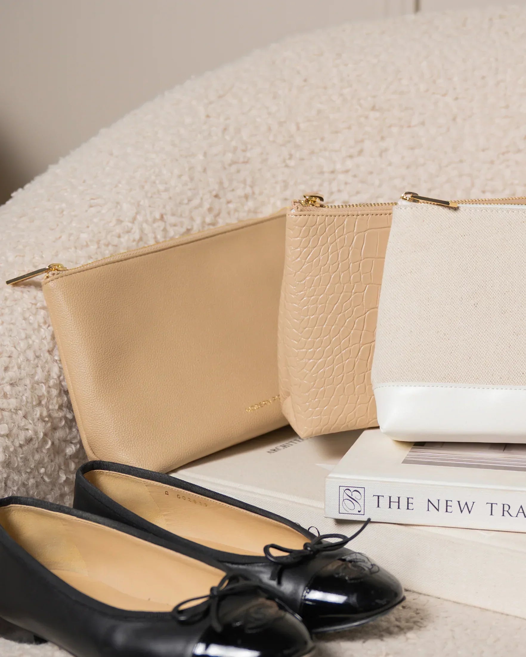 Stylish beige and white vegan leather pouches with gold zippers, paired with black ballet flats on a cozy surface.