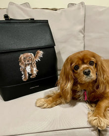 Brown spaniel dog lying near a black insulated lunch bag featuring a dog illustration on a couch.