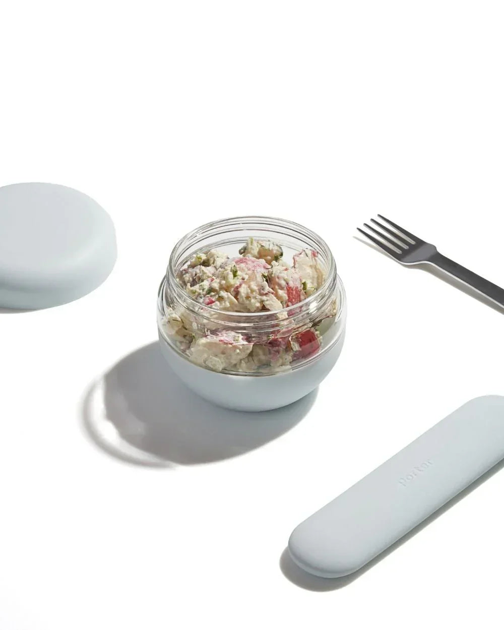 Insulated lunch container with fresh salad, gray lid, fork, and case on white background
