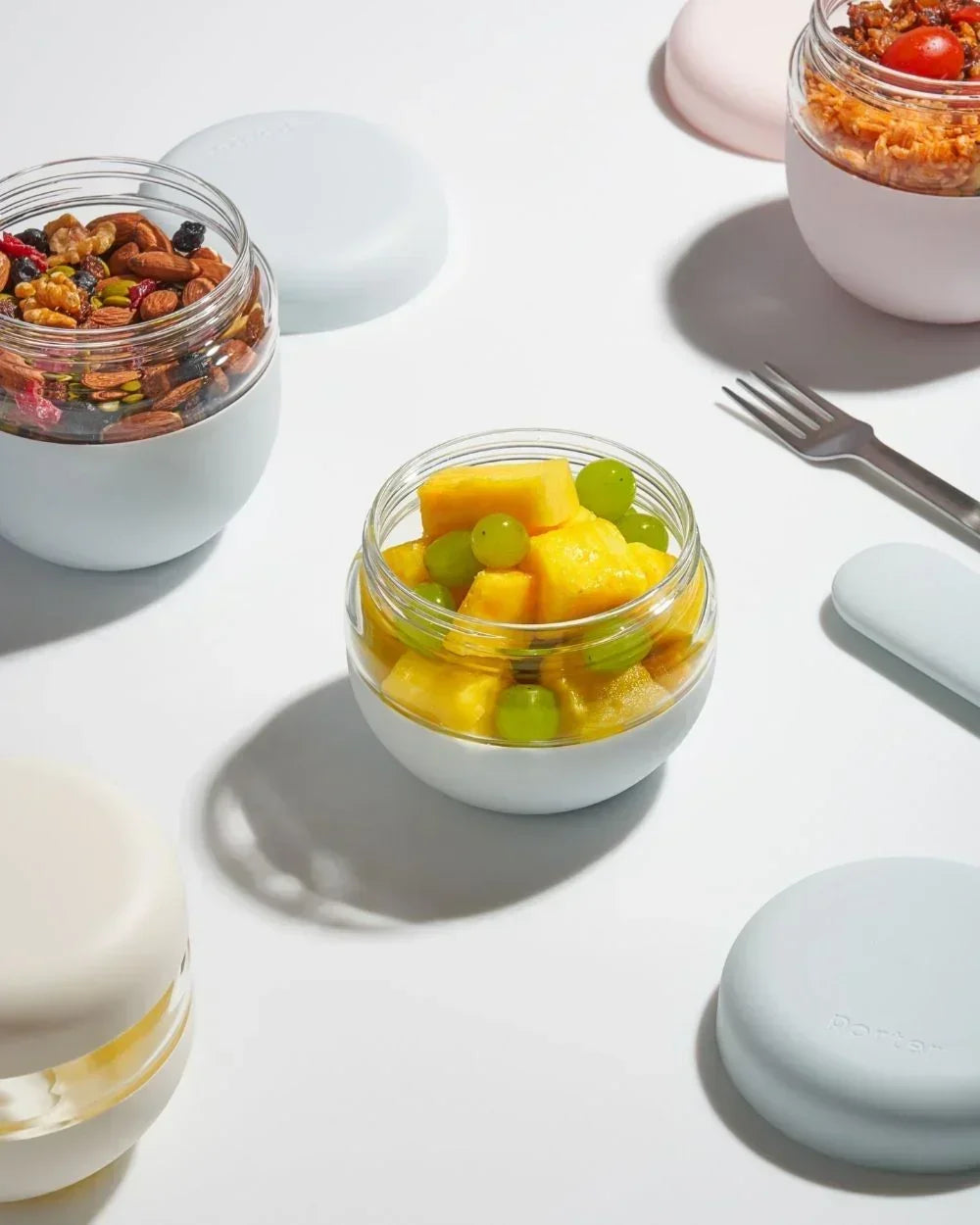 Assorted snacks and lunch foods in modern insulated glass food containers on a white surface