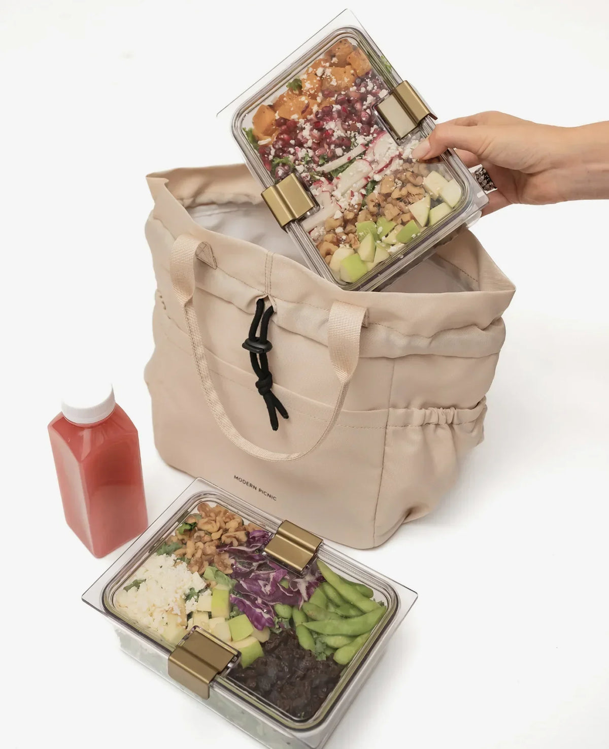 A person placing a clear glass meal prep container into a beige insulated lunch tote bag.