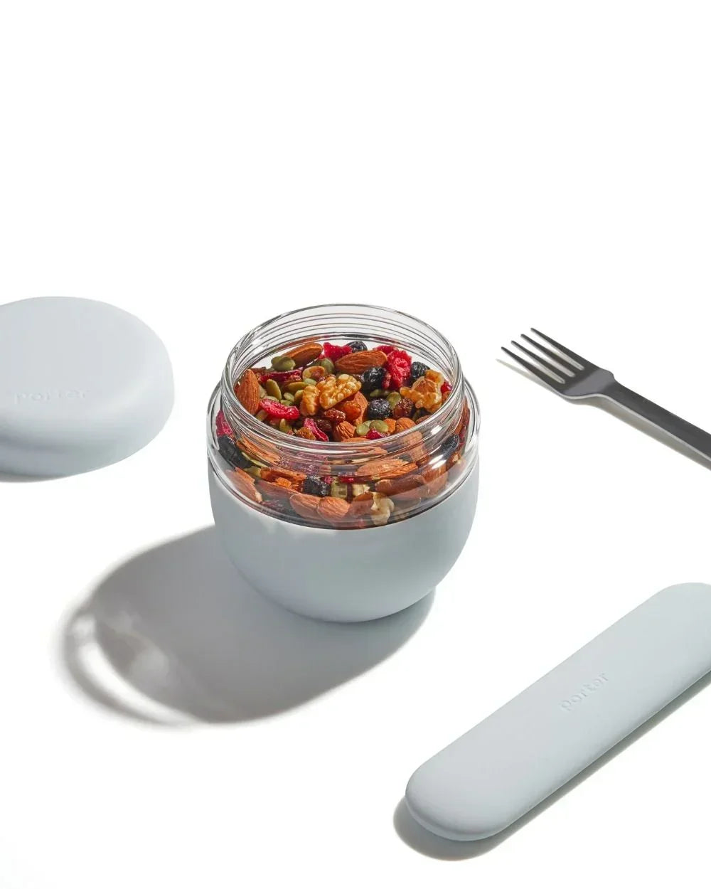 Glass lunch container with mixed nuts and fruit, reusable fork and case on white background