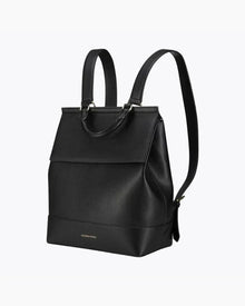 A full-view product photo shot at a side angle of a sleek, structured backpack with top-carry handle and a fold-over flap.