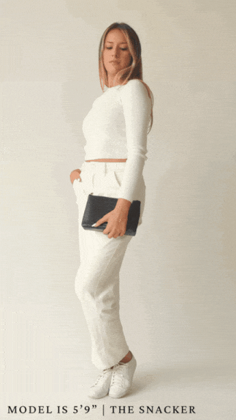 A full-body animation shows a blonde woman wearing a white long-sleeve top and white trousers modeling the small, rectangular pouch.