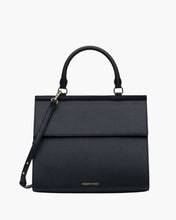 A structured black purse. It features a curved top handle, a fold-over flap closure, a thin, adjustable shoulder strap attached to one side with gold-tone hardware, and the MODERN PICNIC logo subtly stamped in gold near the bottom edge.