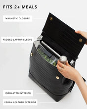 Open view of the black croc-embossed insulated lunch backpack showing a meal container and water bottle inside, highlighting the padded laptop sleeve, magnetic closure, and vegan leather exterior.