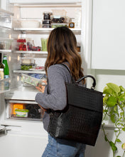 Woman preparing lunch from refrigerator with the black insulated meal prep backpack on her shoulder, showing how it is used for carrying healthy food.