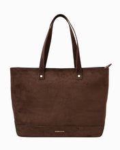 Front view of a rich brown suede tote bag with golden hardware and visible branding logo centered near the base.