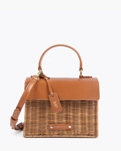 Front view of the Brown Wicker Mini Lunchbox by Modern Picnic, featuring a hand-woven wicker exterior, brown vegan leather flap, top handle, adjustable strap, and gold hardware.