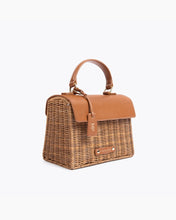 Angled view of the Brown Wicker Mini Lunchbox by Modern Picnic featuring a hand-woven wicker exterior, brown vegan leather flap and top handle, MP tag, and gold hardware.