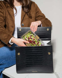 Woman placing glass lunch container with salad into black vegan leather lunch bag