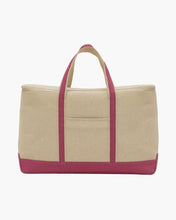 A back view of the large beige canvas cooler tote bag with a pink base and pink accents on the handles. The back features a centered, stitched-in slip pocket.