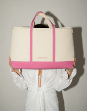 A person wearing a white tie-front shirt holds up a large beige canvas cooler tote bag with a bright pink base and vertical trim, completely obscuring their face. The bag has the small pink text "MODERN PICNIC" on the front.