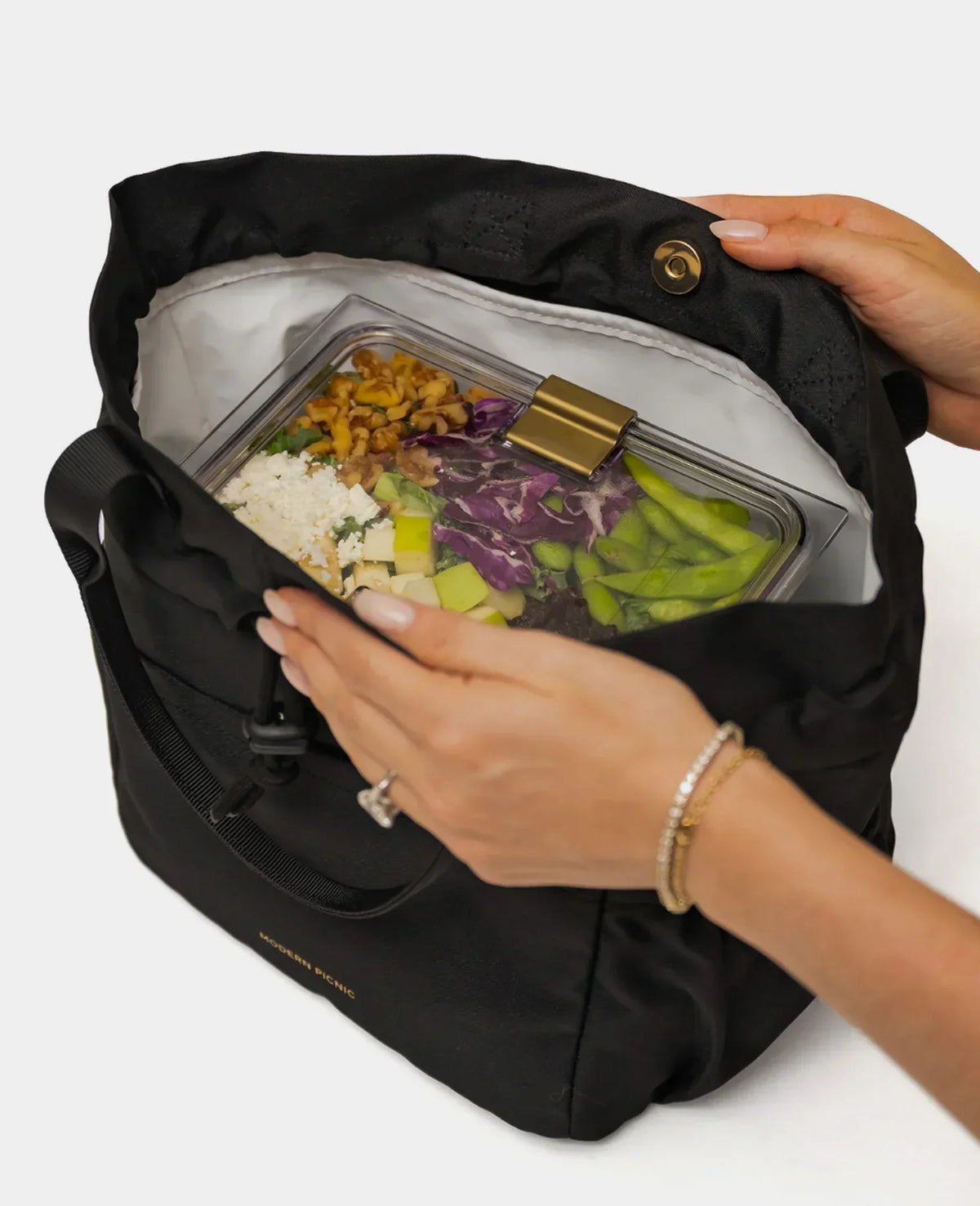 A person packing a healthy salad in a clear glass container inside a black insulated lunch bag.