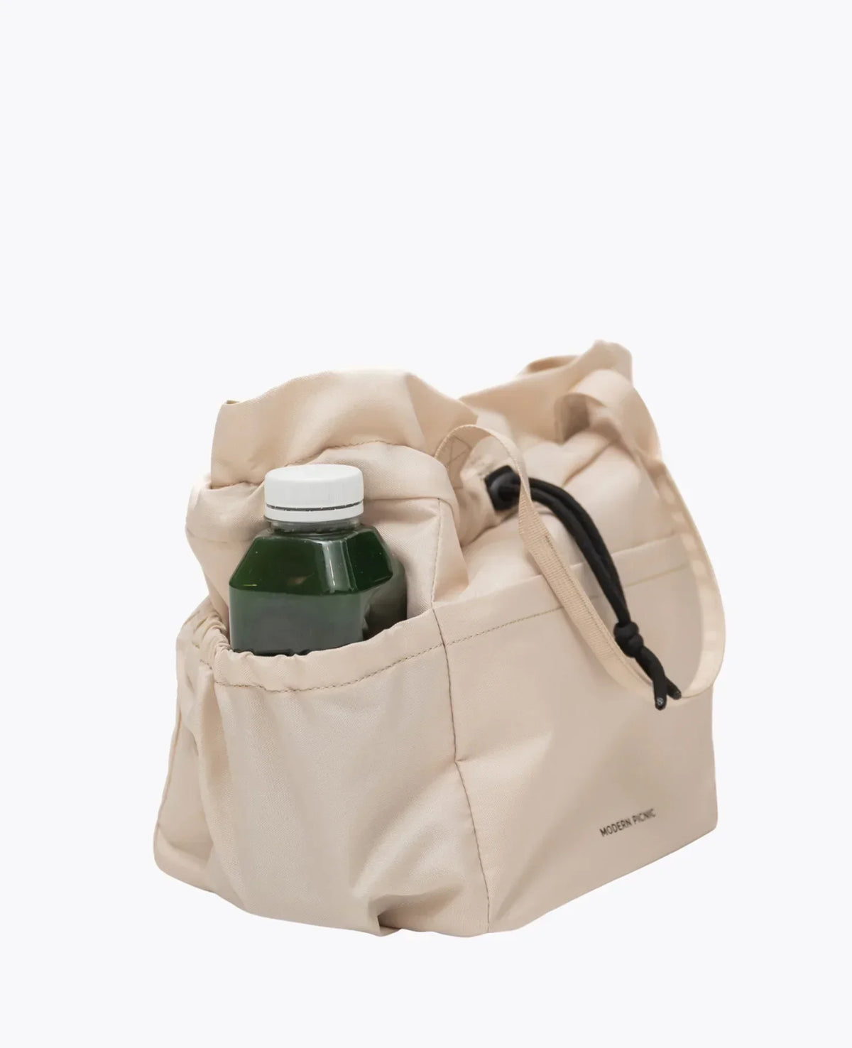 Beige insulated lunch bag from Modern Picnic with a green glass juice bottle inside