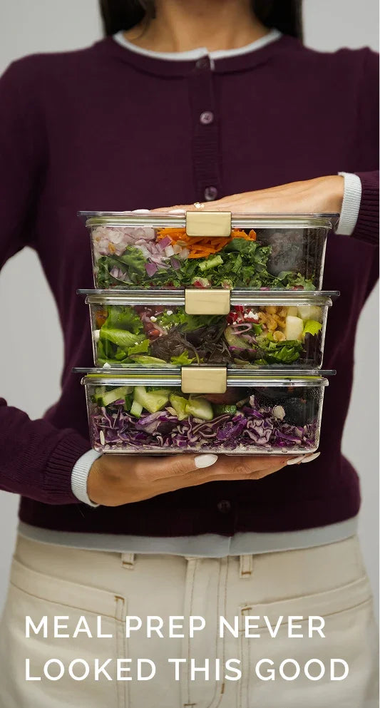 A person holding three stacked glass meal prep containers filled with fresh salads.