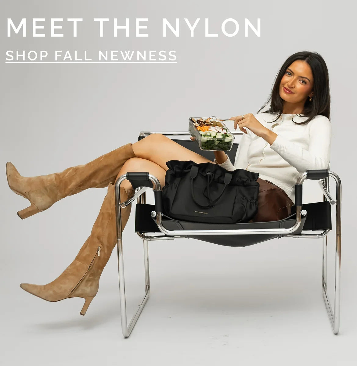 Woman in fall attire relaxing in a chair with a black nylon insulated lunch bag and meal prep container.