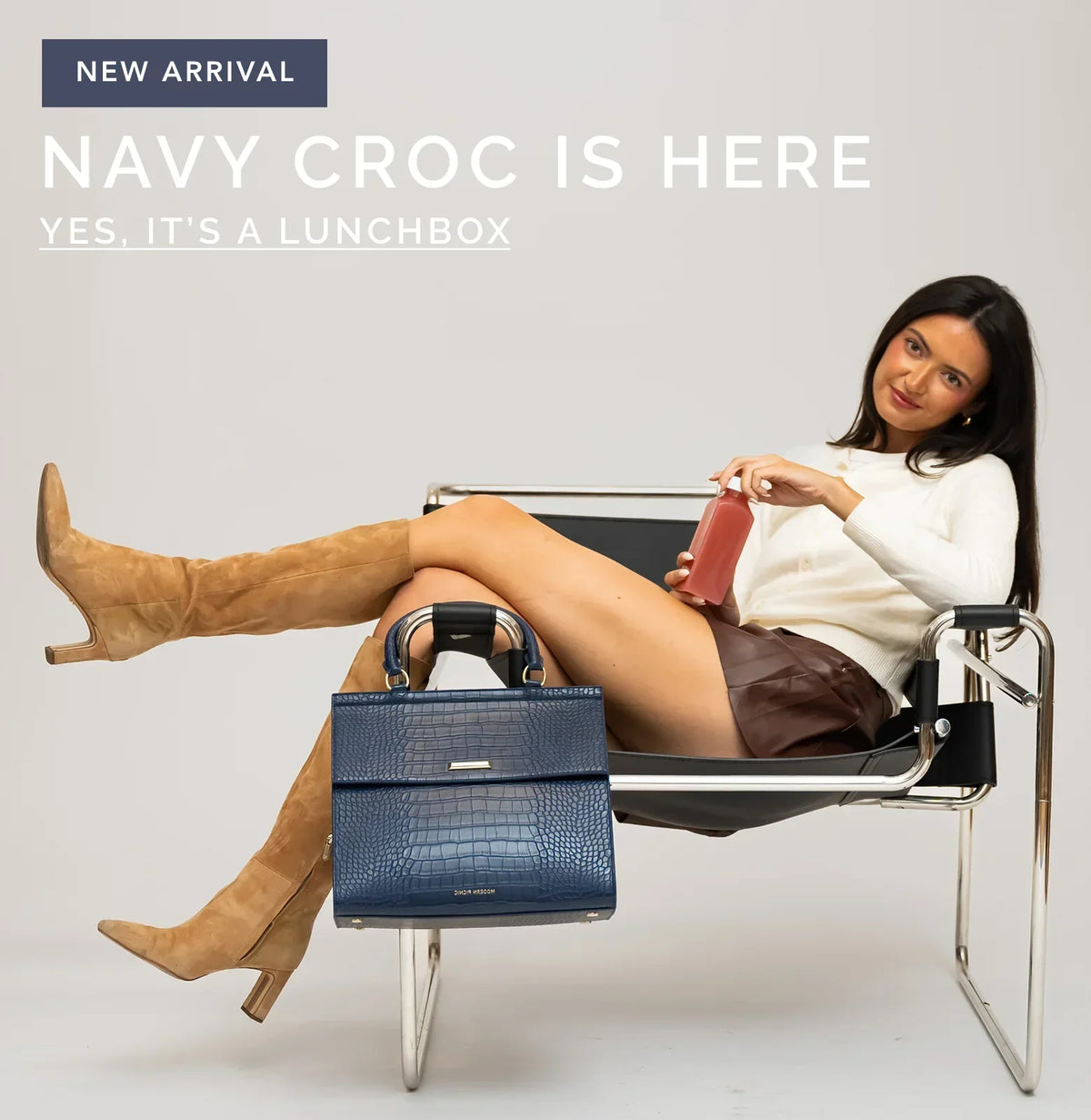 Woman relaxing in a chair with a navy blue croc-embossed insulated lunch bag.
