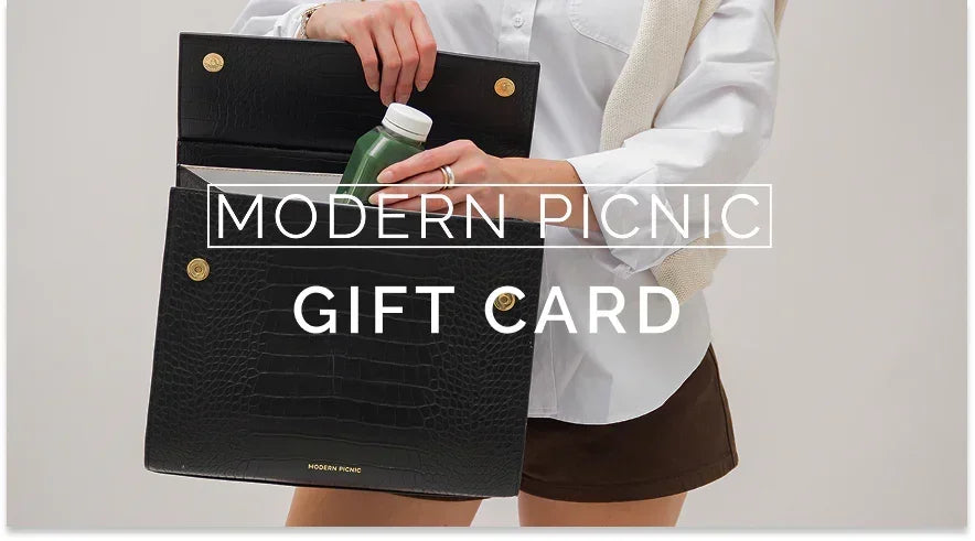 Modern Picnic gift card in black textured lunch bag with gold hardware, held by person in white shirt