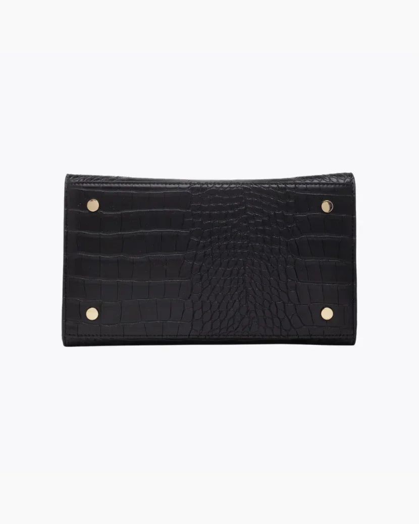 A close-up view of the bottom of the black handbag, showing the flat base with a crocodile-embossed texture. The base is protected by four small gold metal feet (studs).