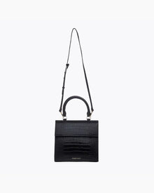 A front-facing studio shot of a structured black handbag made of crocodile-embossed vegan leather. The bag is suspended from its thin, adjustable black shoulder strap, with the top handle and gold hardware visible.