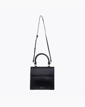 A front-facing studio shot of a structured black handbag made of crocodile-embossed vegan leather. The bag is suspended from its thin, adjustable black shoulder strap, with the top handle and gold hardware visible.