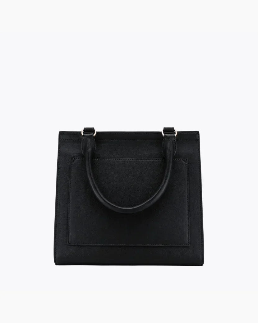 A close-up studio shot showing the back view of a structured black handbag. The bag is made of pebbled vegan leather and features a flat, rectangular stitched-in slip pocket and a single curved top handle attached with gold hardware.