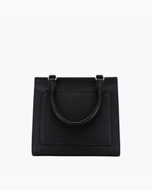 A close-up studio shot showing the back view of a structured black handbag. The bag is made of pebbled vegan leather and features a flat, rectangular stitched-in slip pocket and a single curved top handle attached with gold hardware.