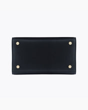 A close-up view of the bottom of the black handbag, showing the flat, structured base made of pebbled vegan leather. The base is protected by four small gold metal feet (studs), one in each corner.