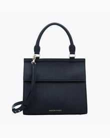 A front-facing studio shot of a structured black top-handle handbag. The bag is made of pebbled vegan leather and features a clean flap closure, a detachable matching shoulder strap, and gold hardware. The logo, "MODERN PICNIC," is subtly visible in gold near the bottom.