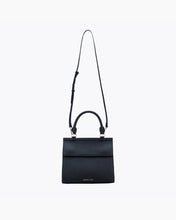 A front-facing studio shot of a structured black handbag made of pebbled vegan leather. The bag is suspended from its thin, adjustable black shoulder strap, with the top handle and gold hardware visible. The gold "MODERN PICNIC" logo is visible near the bottom.