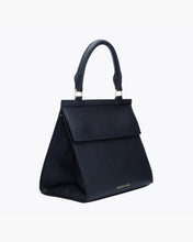 A three-quarter studio shot of a structured black top-handle handbag. The bag is made of pebbled vegan leather and has a curved top handle, a prominent flap closure, and gold hardware. The gold "MODERN PICNIC" logo is visible near the bottom front edge.