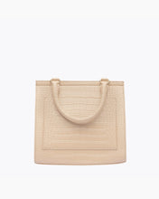 A close-up studio shot showing the back view of a structured light beige handbag. The bag is made of crocodile-embossed vegan leather and features a stitched-in slip pocket outline and a single curved top handle attached with gold hardware.