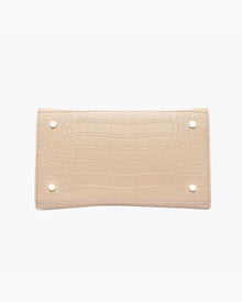 A close-up view of the bottom of the light beige handbag, showing the flat base with a crocodile-embossed texture. The base is protected by four small gold metal feet (studs).