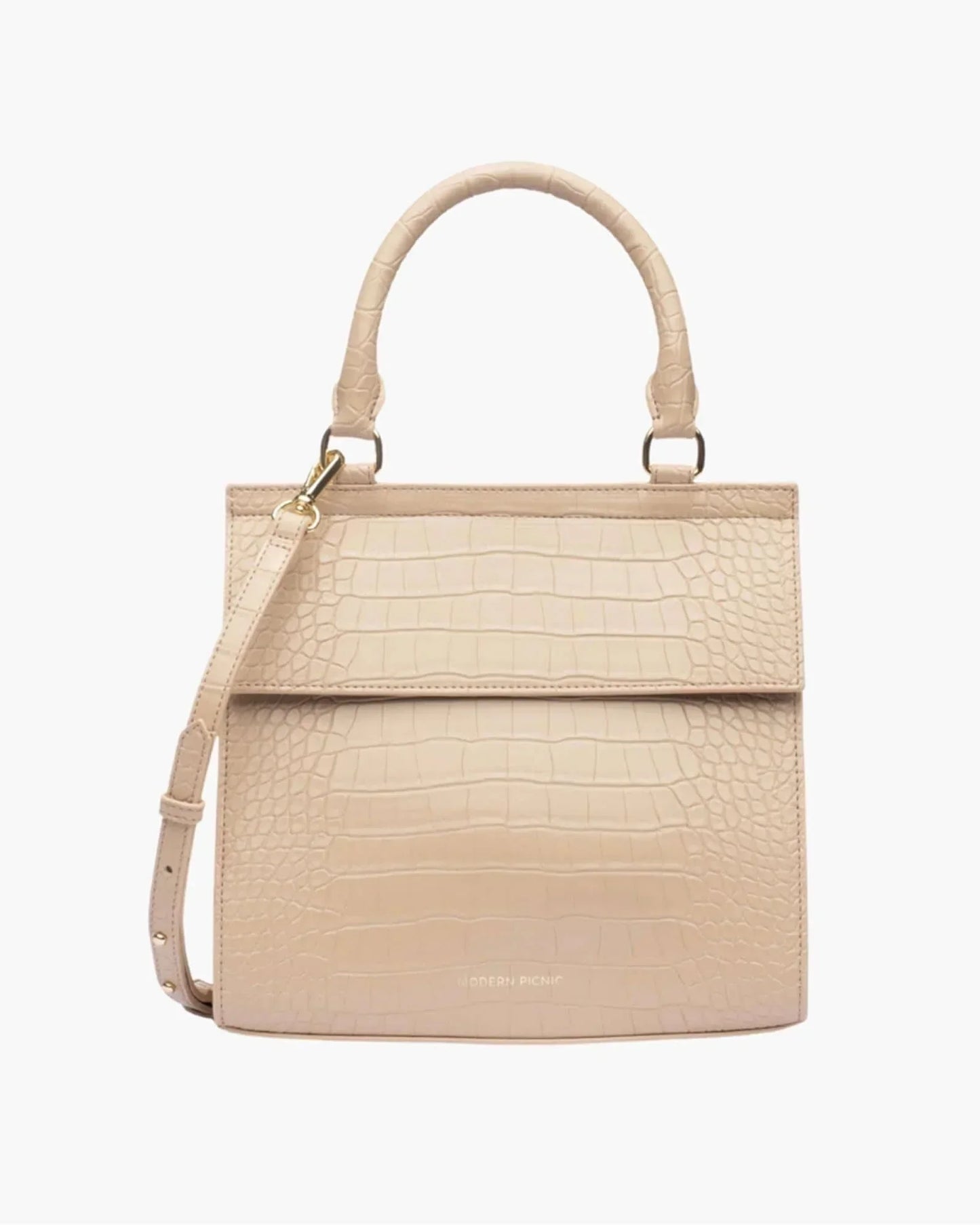 A front-facing studio shot of a structured, light beige top-handle handbag. The bag is covered in a crocodile-embossed texture and features a clean flap closure, a detachable shoulder strap, and gold hardware. The logo "MODERN PICNIC" is subtly visible in gold near the bottom.