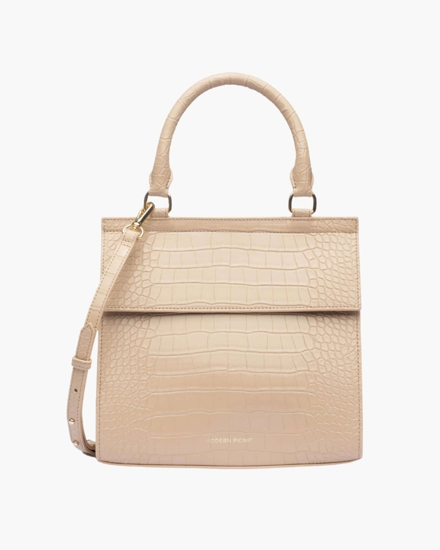 A front-facing studio shot of a structured, light beige top-handle handbag. The bag is covered in a crocodile-embossed texture and features a clean flap closure, a detachable shoulder strap, and gold hardware. The logo 