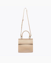 A front-facing studio shot of a structured light beige handbag made of crocodile-embossed vegan leather. The bag is suspended from its thin, adjustable strap, with the top handle and gold hardware visible.