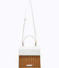 A front-facing studio shot of a two-toned small handbag suspended from its thin, white adjustable shoulder strap. The top section is smooth white vegan leather, and the bottom is natural brown woven wicker. The bag has a white hang tag with gold "MP" initials and a white logo plaque on the wicker.