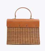 A back view of the structured picnic-style handbag. The bottom two-thirds of the bag are made of brown woven wicker, and the top flap is smooth brown vegan leather. The back of the leather flap is secured to the wicker body with four visible gold-tone fasteners.