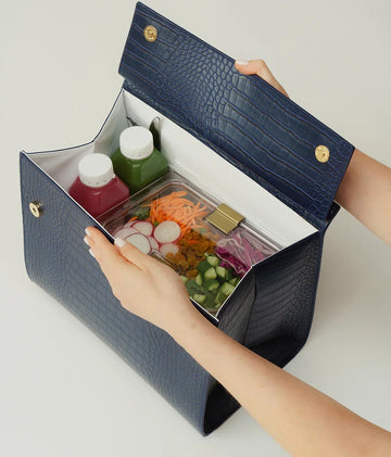 Navy blue vegan leather insulated lunch bag filled with fresh salads and juices.