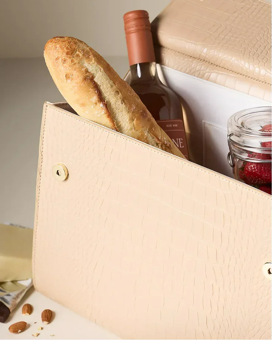 Cream croc-embossed insulated lunch bag with baguette, wine, jar of berries, and cheese inside