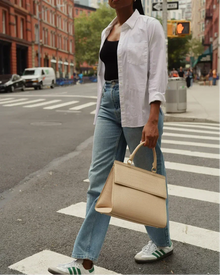 Woman crossing city street holding cream-colored croc-embossed vegan leather lunch bag