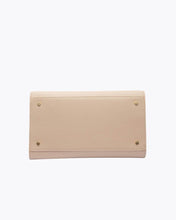 A view of the bottom of the cream-colored handbag, showing the flat base with four small gold metal feet (studs) designed to protect the material.