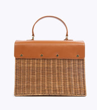 A back view of the structured picnic-style handbag. The bottom two-thirds of the bag are made of brown woven wicker, and the top flap is smooth brown vegan leather. The back of the leather flap is secured to the wicker body with four visible gold-tone fasteners.
