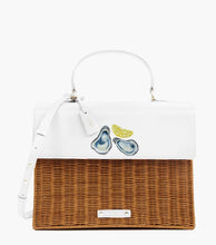 A front-facing studio shot of a structured top-handle handbag with a picnic aesthetic. The bag features a white vegan leather top flap with a hand-painted design of two oysters on the half shell and a yellow lemon slice. The bottom section of the bag is made of brown woven wicker. It has a white handle, a white shoulder strap, a white hang tag with gold "MP" initials, and a small white logo plaque on the wicker.