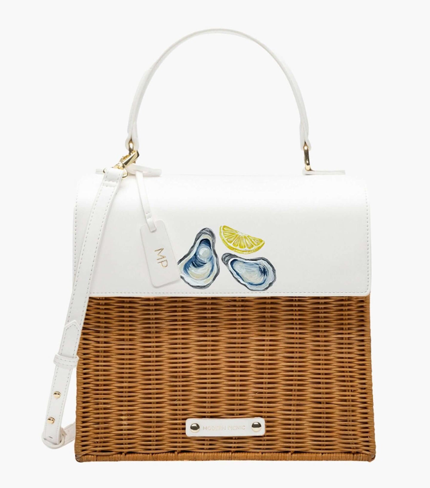 A front-facing studio shot of a structured top-handle handbag with a coastal design. The top white vegan leather flap is decorated with a hand-painted design of two oysters on the half shell and a lemon slice. The bottom section of the bag is made of natural brown woven wicker. It features a white hang tag with gold 