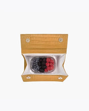 Top-down view of the Marigold Croc Kids Mini by Modern Picnic, shown open to reveal its insulated interior holding a clear food container filled with fresh berries, including blueberries, blackberries, and raspberries. The marigold croc-embossed vegan leather exterior and magnetic snap closures are visible against a white background.
