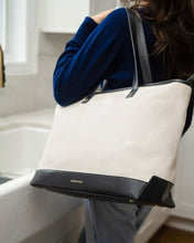 Woman carrying Modern Picnic canvas tote with black vegan leather trim, a chic and functional work or travel bag.
